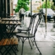 Verregnete Stühle und Tische eines Restaurants in einer städtischen Straße.