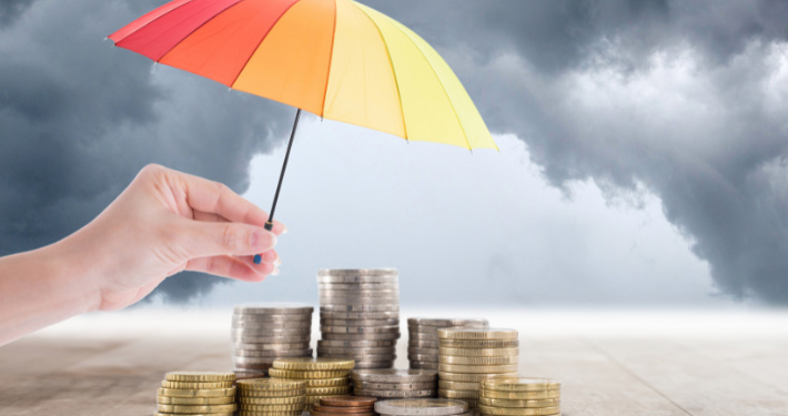 Hand halt einen bunten Regenschirm, um die Münzen darunter vor dem aufziehenden Gewitter zu schützen