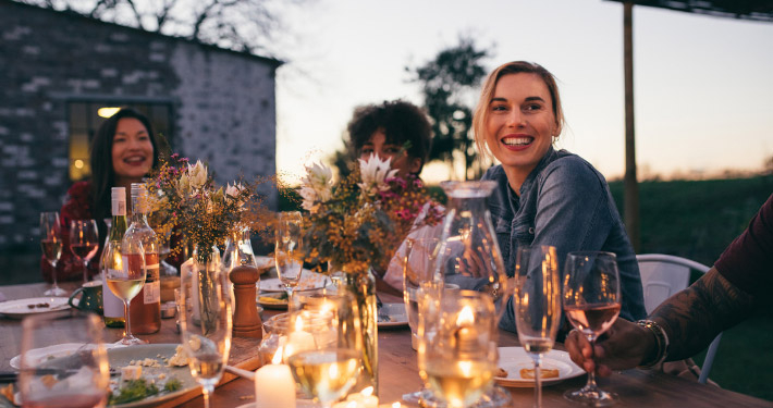 Gäste in der Abenddämmerung auf einer Restaurant-Terrasse mit Speisen und Getränken auf dem Tisch