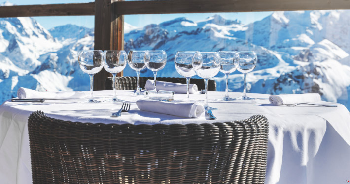 Acht Weingläser stehen auf einem Tisch einer Restaurantterrasse im Winter bei strahlendem Sonnenschein